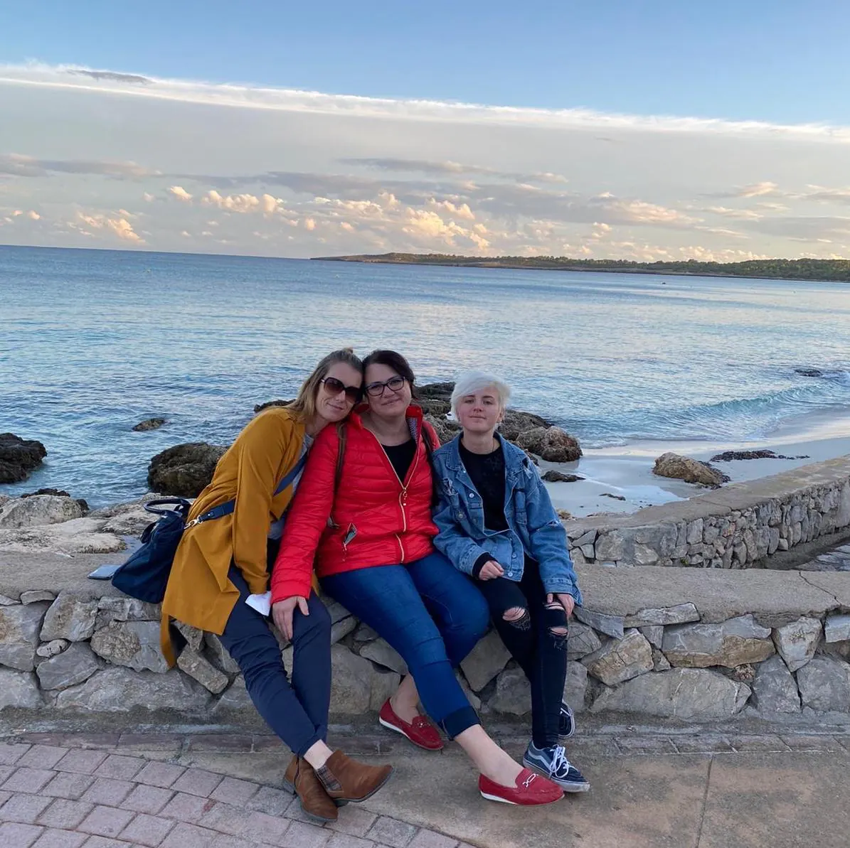 Drei Frauen sitzen auf einer Mauer am Meer